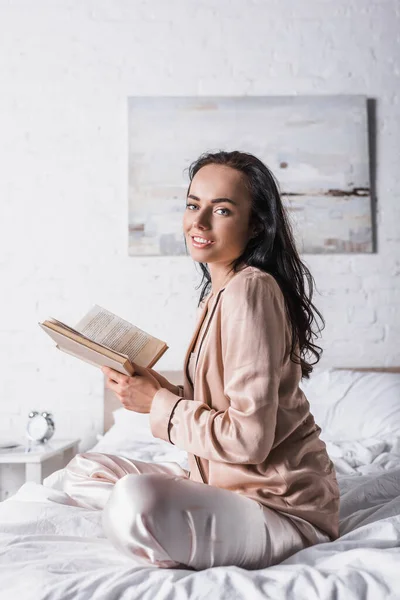 Junge brünette Frau sitzt morgens mit Buch im Bett — Stockfoto