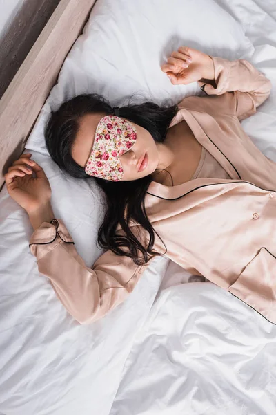 Top view of young brunette woman sleeping in bed in sleep mask — стоковое фото