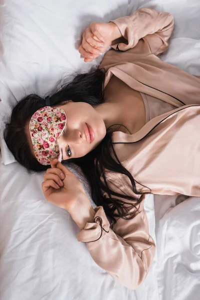 Vue du dessus de la jeune femme brune couchée au lit dans un masque de sommeil — Photo de stock