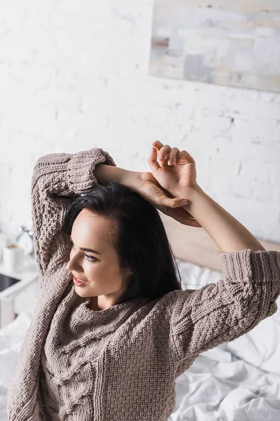 Молодая брюнетка в свитере сидит в постели по утрам — стоковое фото