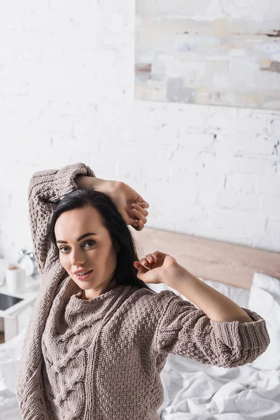 Young brunette woman in sweater sitting in bed at morning — Stock Photo