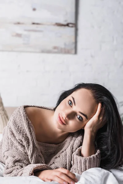 Young brunette woman in sweater lying in bed at morning — Stock Photo