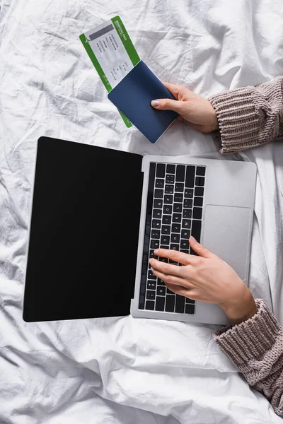 Top view of woman in sweater lying in bed with laptop and air ticket — Stock Photo