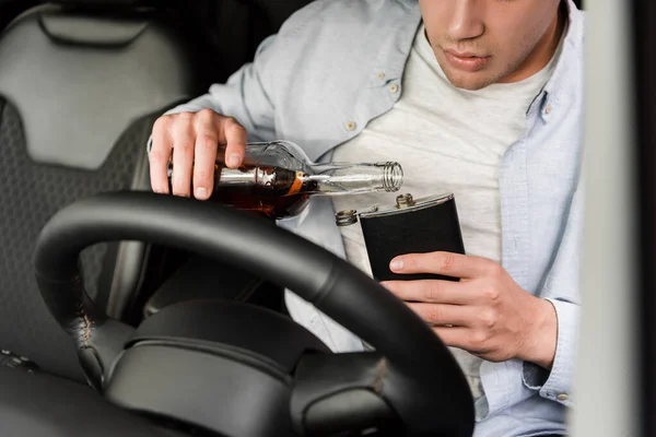 Cropped view of man pouring whiskey from bottle to flask in car, blurred foreground — Stock Photo