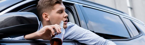 Drunk man holding bottle of alcohol while looking out car window, banner — Stock Photo