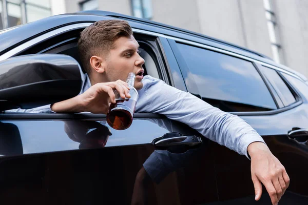 П'яний чоловік дивиться вікно машини, тримаючи пляшку віскі — стокове фото