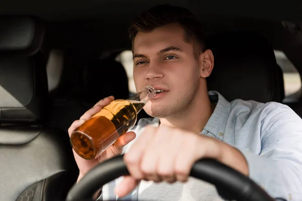 Young man drinking whiskey while driving car on blurred foreground — Stock Photo