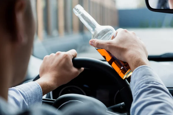 Vista parcial del hombre que conduce el coche mientras sostiene la botella de whisky, primer plano borroso - foto de stock