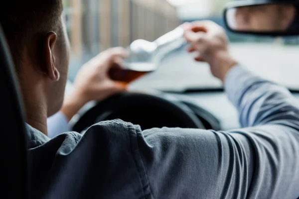 Partial view of man opening bottle of alcohol in car, blurred foreground — Stock Photo