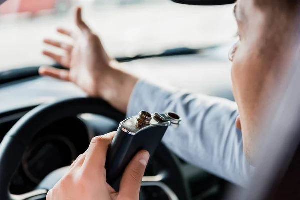 Vista recortada del hombre haciendo gestos y sosteniendo frasco con alcohol mientras conduce el coche, borrosa primer plano - foto de stock