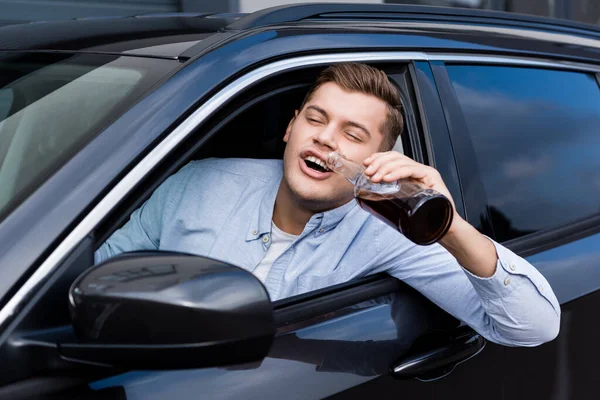 П'яний чоловік п'є віскі, дивлячись на вікно машини — стокове фото