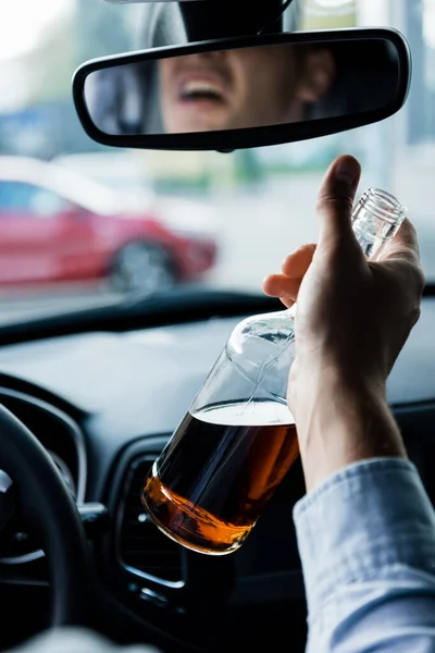 Partial view of drunk man driving car and holding bottle of whiskey, blurred foreground — Stock Photo