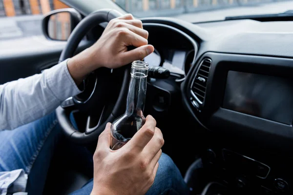 Vista parziale di uomo in possesso di bottiglia di whisky durante la guida di auto — Foto stock