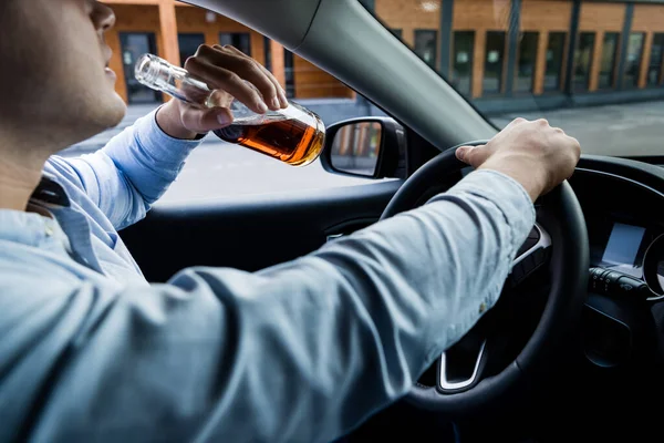Cropped view of man drinking whiskey while driving car, blurred foreground — Stock Photo