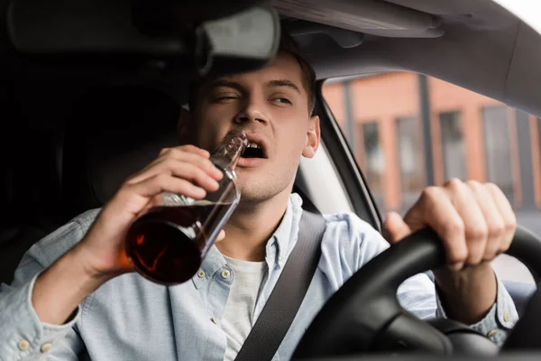 Пьяный мужчина водит машину и пьет виски на размытом переднем плане — стоковое фото