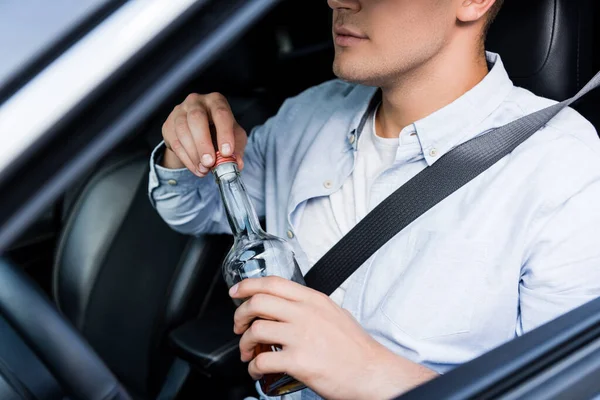 Vista cortada do homem abrindo garrafa de álcool enquanto sentado no assento do motorista no carro, foreground borrado — Fotografia de Stock