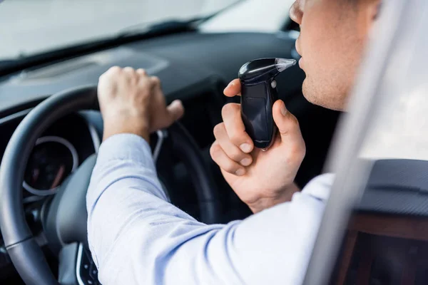 Vista parziale del conducente che soffia nell'etilometro in auto, primo piano sfocato — Foto stock