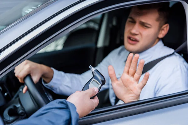 Poliziotto dando etilometro al conducente ubriaco mostrando gesto di rifiuto, sfondo sfocato — Foto stock