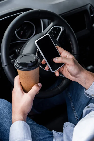 Cropped view of man holding coffee to go and smartphone with blank screen near steering wheel — Stock Photo