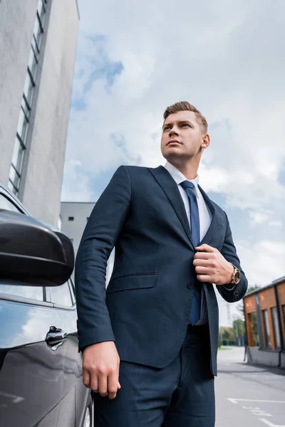 Joven empresario confiado desabotonar chaqueta mientras está de pie cerca de coche - foto de stock