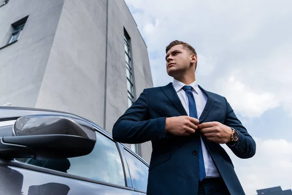 Low angle view of businessman buttoning up blazer near car — Stock Photo