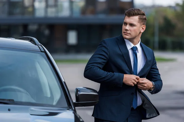 Geschäftsmann knöpft Blazer neben Auto zu, verschwommener Vordergrund — Stockfoto