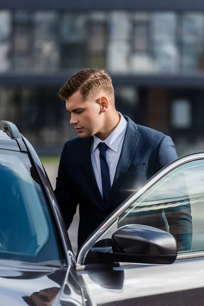 Joven hombre de negocios de pie cerca de auto con puerta abierta al aire libre - foto de stock