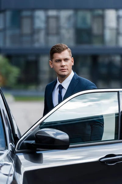 Jeune homme d'affaires debout près de la voiture avec porte ouverte — Photo de stock