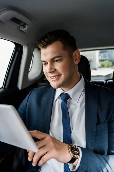 Усміхнений бізнесмен, використовуючи цифровий планшет на розмитому передньому плані в машині — стокове фото