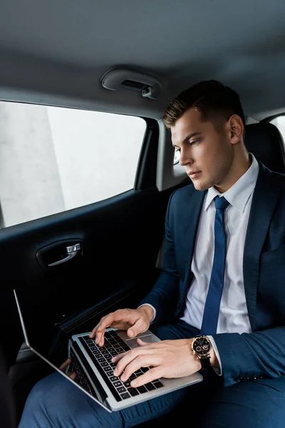 Empresário em desgaste formal usando laptop no banco de trás do carro — Fotografia de Stock