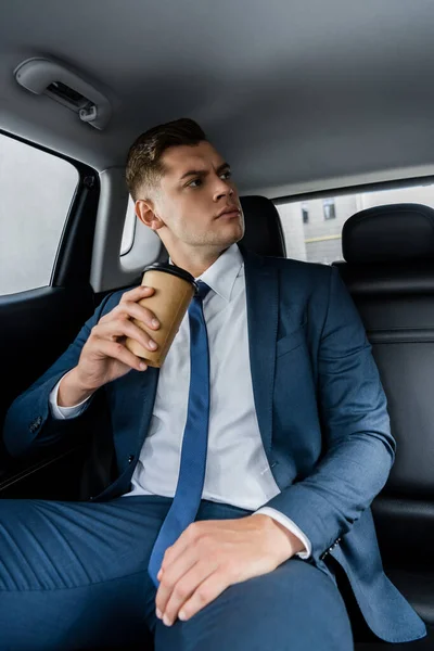Hombre de negocios confiado sosteniendo café para ir en el asiento trasero del coche - foto de stock