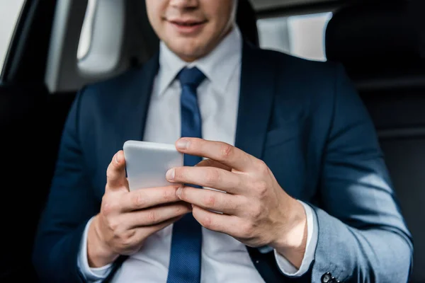 Vista recortada del teléfono inteligente en manos de hombre de negocios sobre fondo borroso en auto - foto de stock