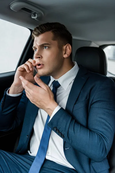 Worried businessman in suit talking on smartphone in car — Stock Photo