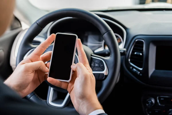 Cropped view of man holding smartphone with blank screen near steering wheel in car on blurred background — Stock Photo