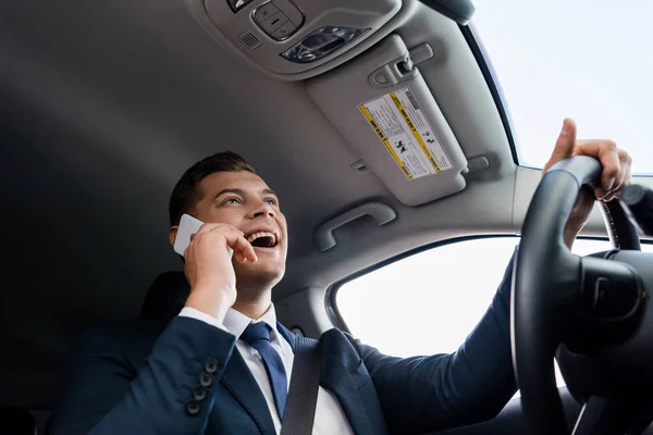 Visão de baixo ângulo do homem positivo em terno falando no celular enquanto dirige o carro — Fotografia de Stock