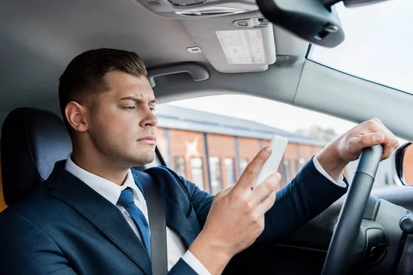 Concentrated businessman using smartphone while driving car — Stock Photo