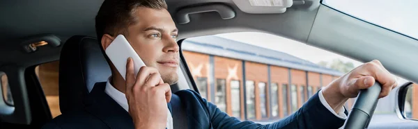Молодой бизнесмен в костюме водит машину и разговаривает на смартфоне, баннере — стоковое фото