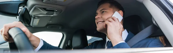 Positiver Geschäftsmann, der während der Autofahrt auf unscharfem Vordergrund mit dem Handy spricht, Banner — Stockfoto