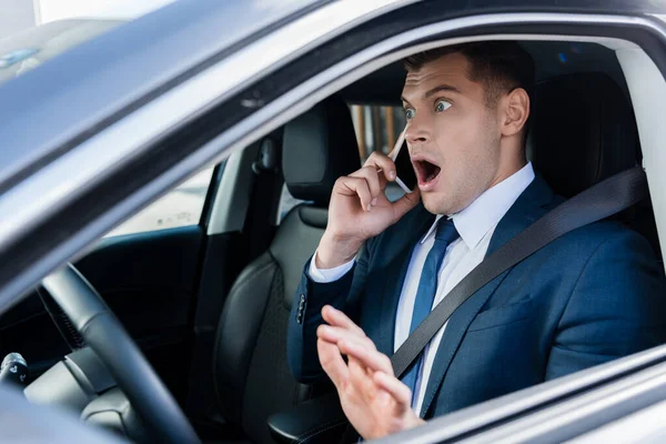 Hombre de negocios asustado hablando en el teléfono inteligente en el asiento del conductor del coche - foto de stock