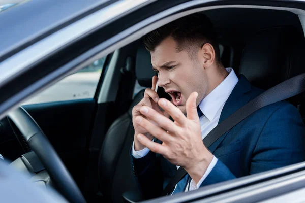 Злий бізнесмен розмовляє на смартфоні в машині на розмитому передньому плані — стокове фото