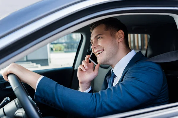 Uomo d'affari sorridente che parla su smartphone mentre guida auto in primo piano sfocato — Foto stock