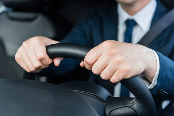 Cropped view of hands of businessman on steering wheel in car — Stock Photo