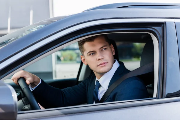 Hombre de negocios mirando a la ventana mientras conduce auto en primer plano borroso - foto de stock