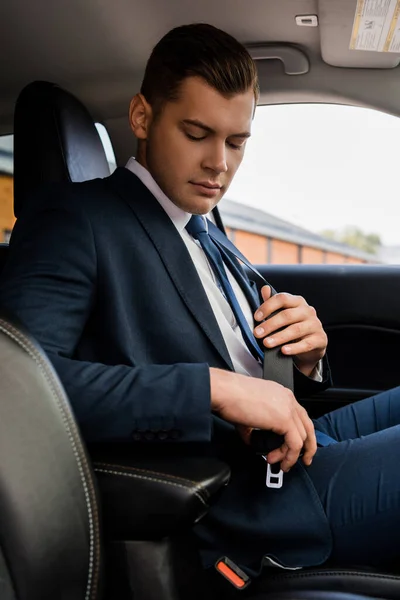 Homme d'affaires tenant la ceinture de sécurité sur le siège du conducteur dans la voiture — Photo de stock