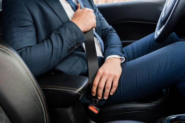 Vista recortada del hombre de negocios que cierra el cinturón de seguridad en el coche en primer plano borroso - foto de stock