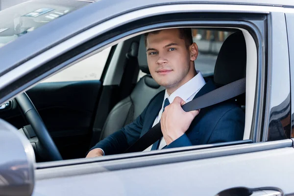 Empresário em desgaste formal segurando cinto de segurança no carro e olhando para a câmera — Fotografia de Stock