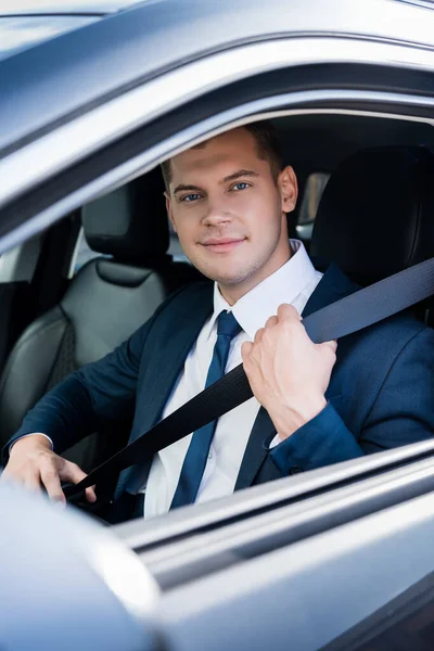 Молодий бізнесмен дивиться на камеру, тримаючи ремінь безпеки в авто — стокове фото