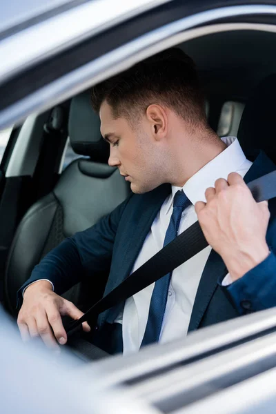 Junger Geschäftsmann im Anzug hält Sicherheitsgurt im Auto im verschwommenen Vordergrund — Stockfoto