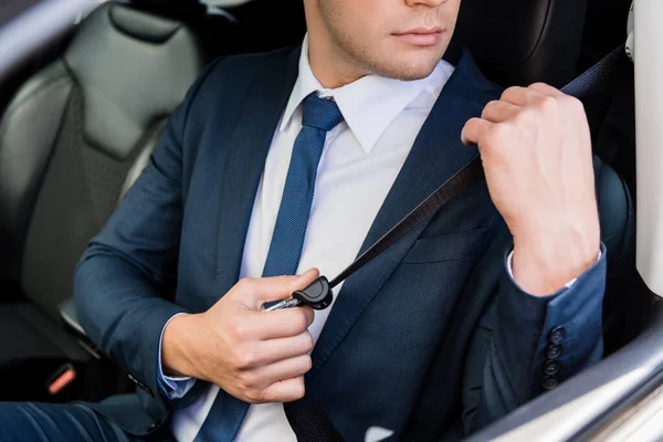 Vista recortada del hombre de negocios ajustando el cinturón de seguridad en el coche sobre fondo borroso - foto de stock