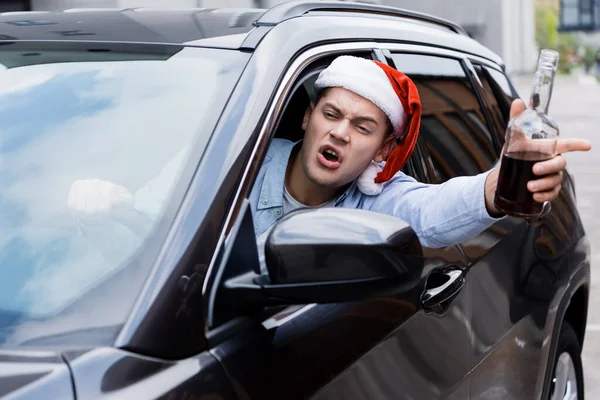 Bêbado, homem zangado em Papai Noel, com garrafa de uísque, olhando pela janela enquanto dirigia carro — Fotografia de Stock